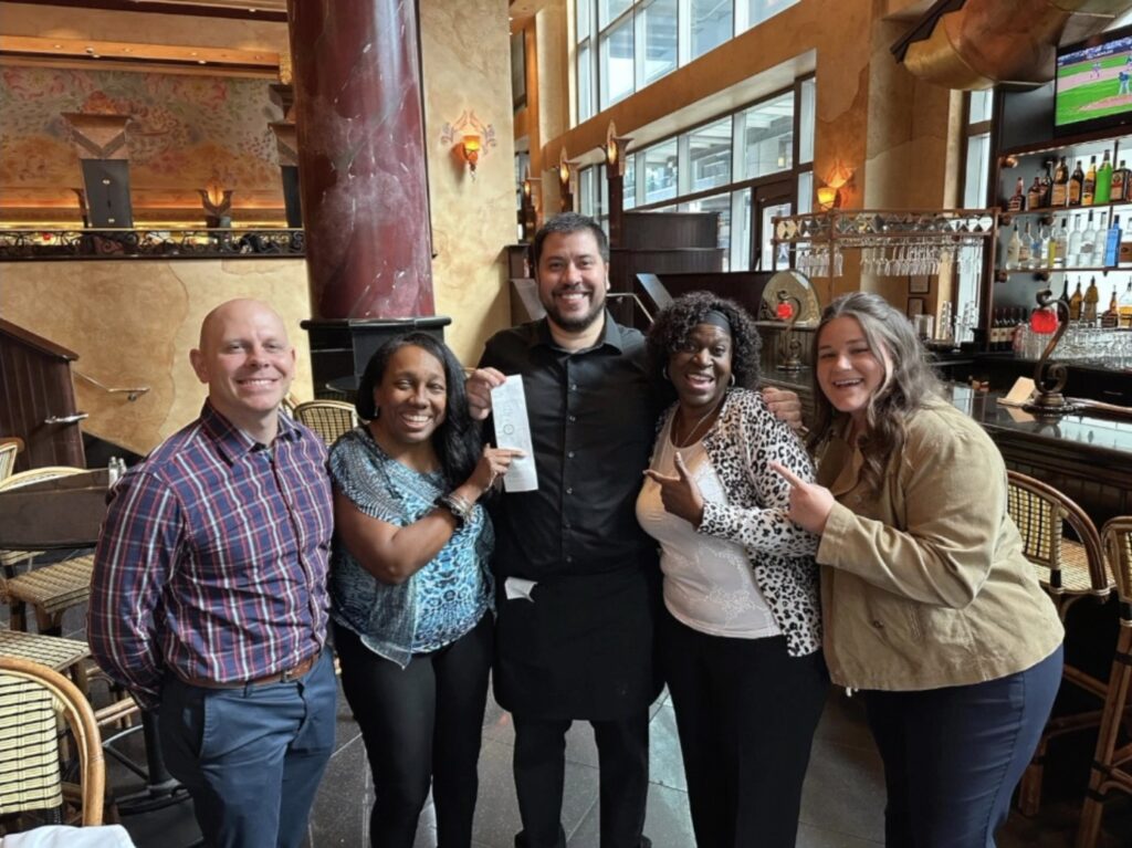 Five people smiling holding a receipt with a $1,000 tip