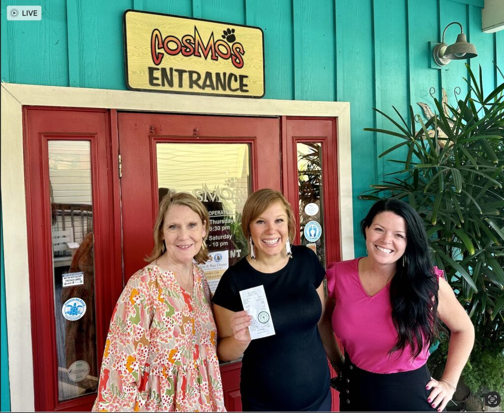 Three women standing in front of the entrance to Cosmo's restaurant. The one in the middle is pregnant and holding a receipt that has a $1,000 tip.